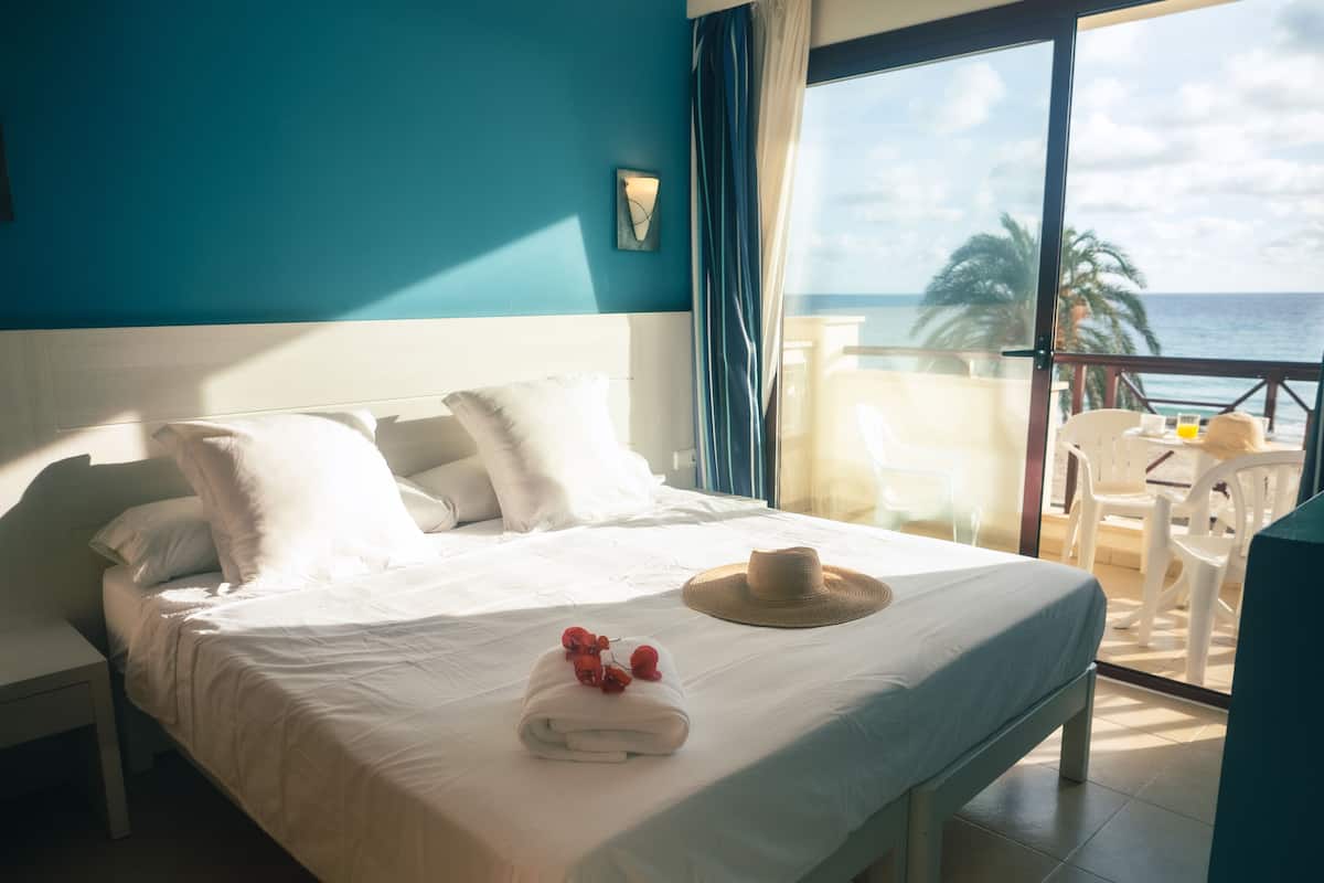 A hotel room with a large bed, a view of the ocean, and a balcony with a table and chairs.
