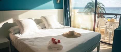 A hotel room with a large bed, a view of the ocean, and a balcony with a table and chairs.