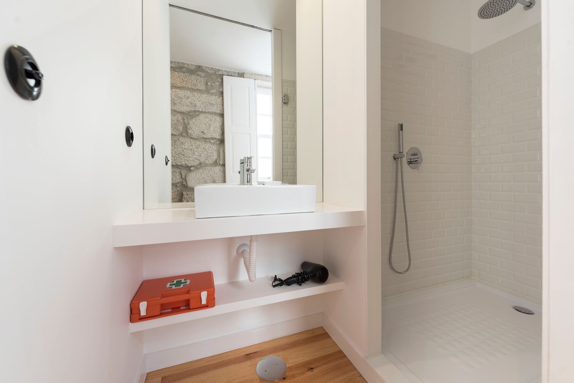 Ein modernes Badezimmer mit einem weißen Waschbecken, einem Spiegel, einer Dusche und einem Holzboden.
