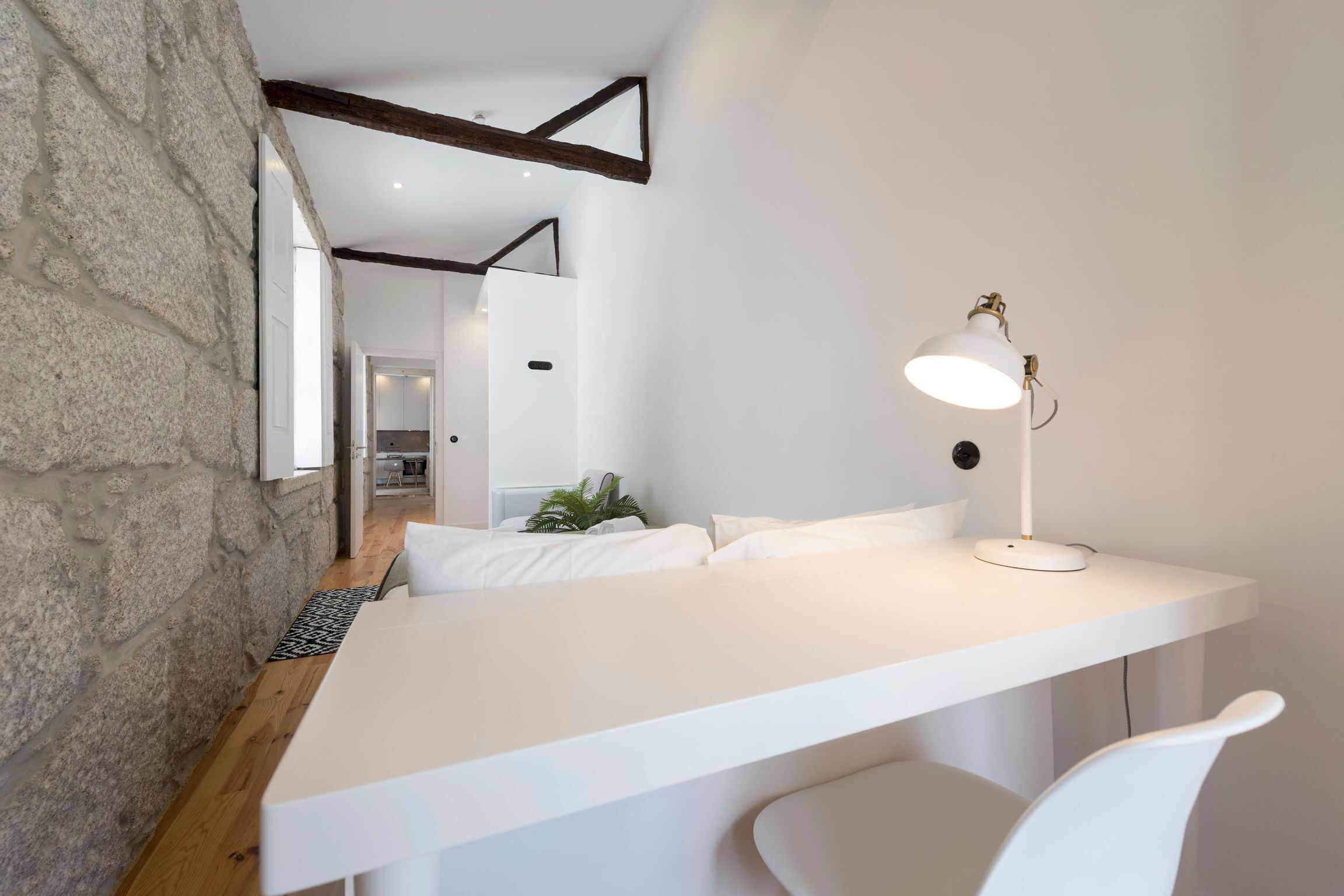 Une chambre à coucher moderne avec un lit blanc, une table de chevet avec une lampe et un mur en pierre.