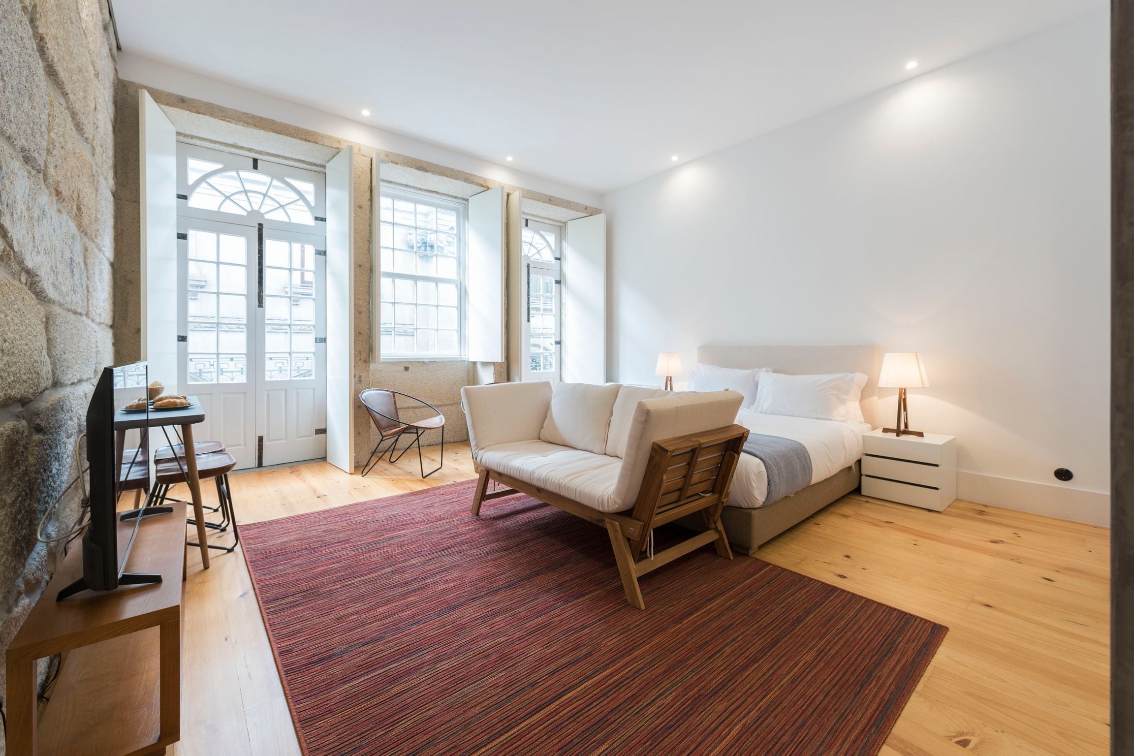 A bedroom with a bed, bedside tables, a chair, a desk, and a TV.
