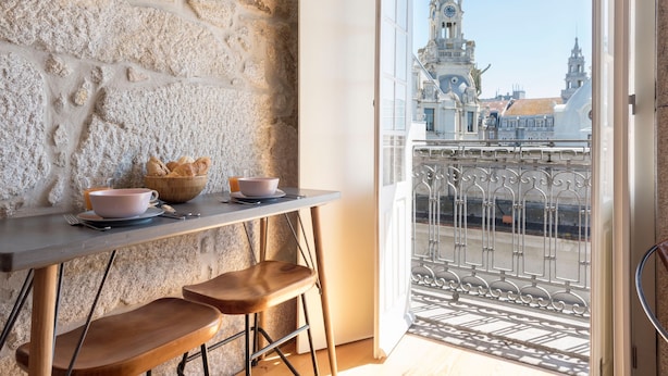 A balcony with a stone wall, a table with a bowl of bread, and a view of a historic building with a clock tower. - Almada 91 (Porto)