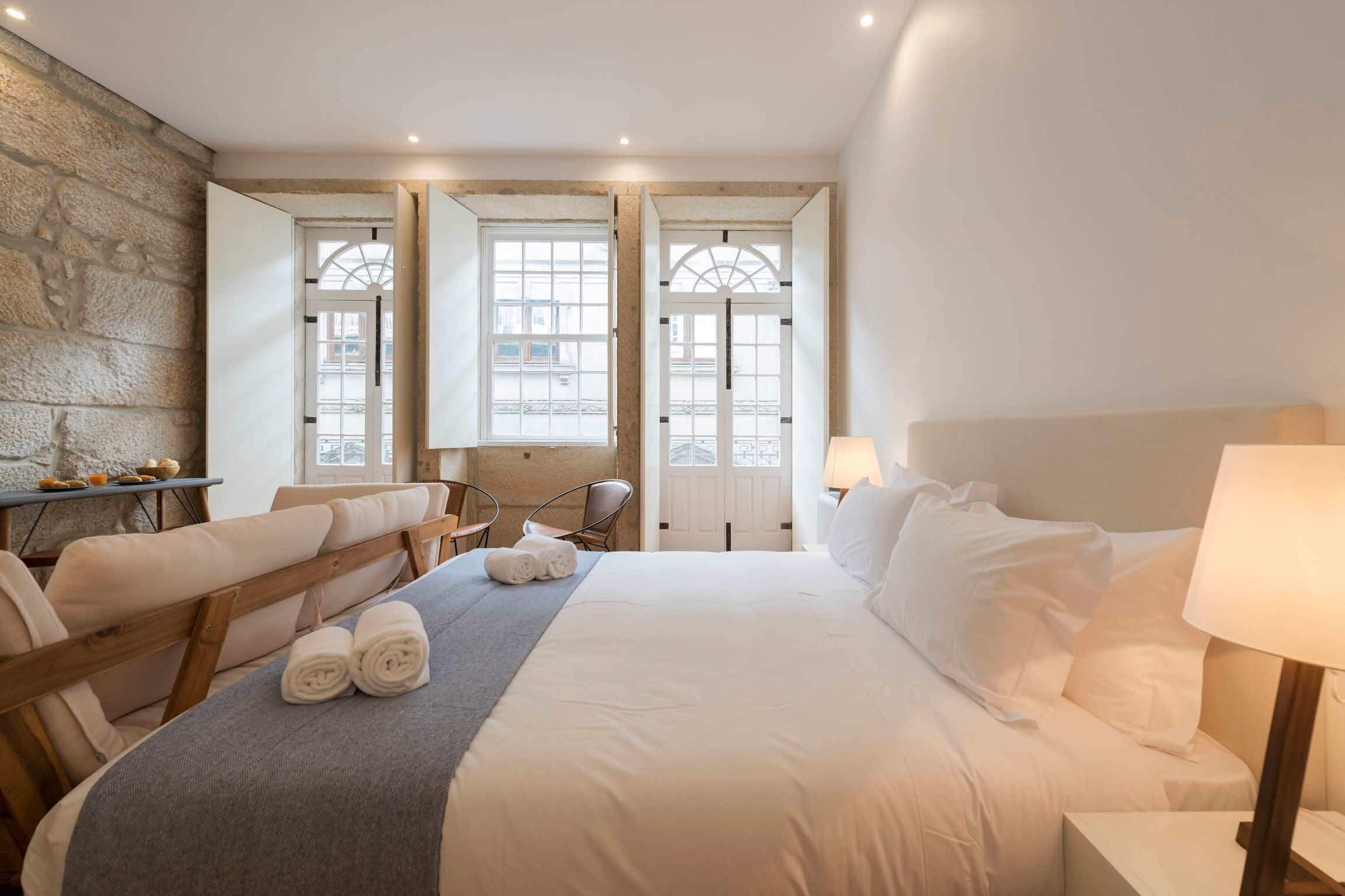 A hotel room with a large bed, two chairs, a small table with bowls, and a mirror on the wall.
