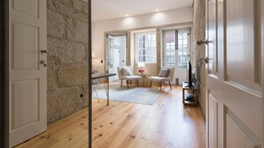 A modern room with a stone wall, wooden flooring, a dining area with chairs and a table, and large windows. - Almada 91 (Porto)