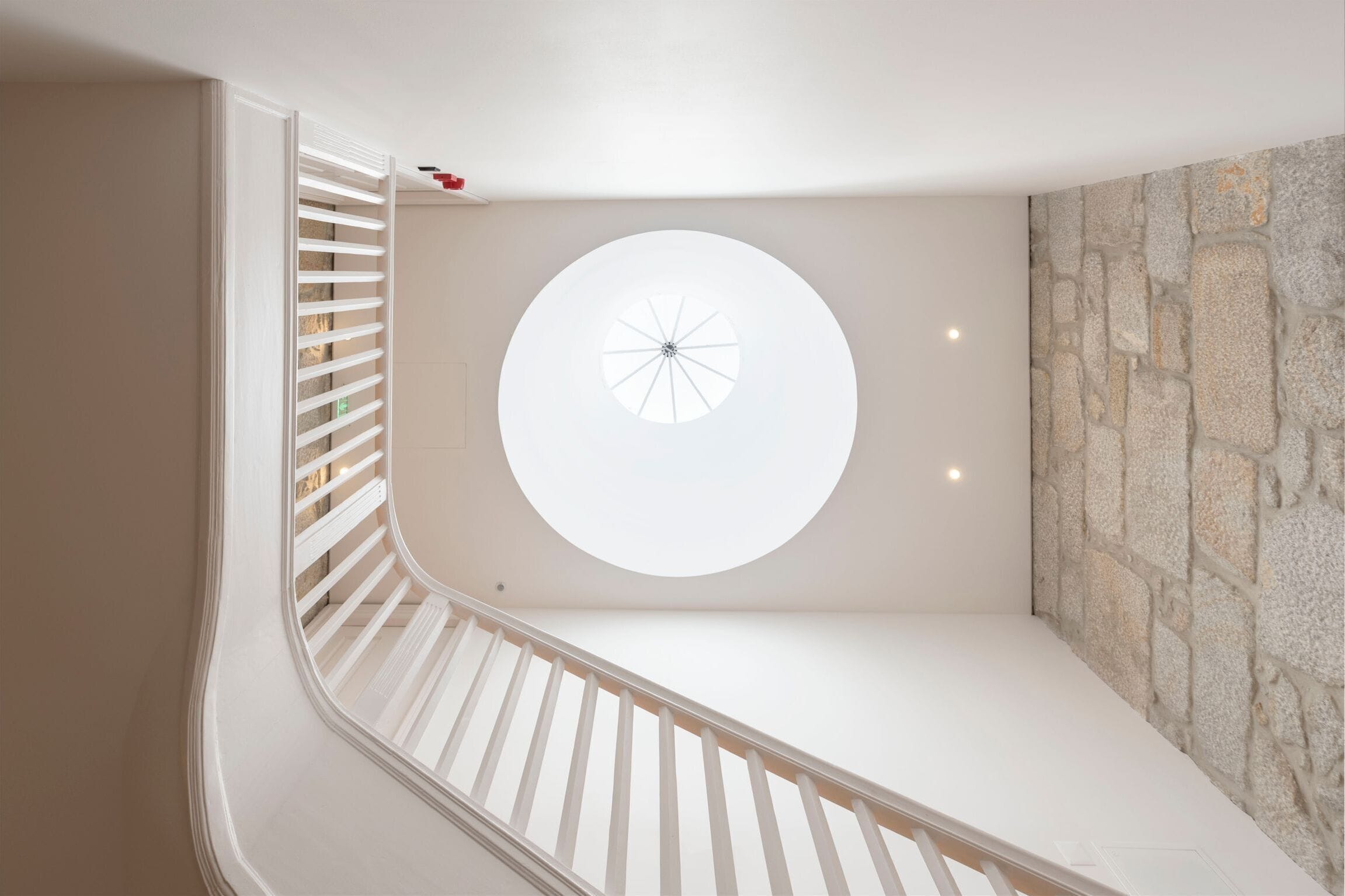 Uma escadaria moderna com um claraboia circular e uma parede de pedra.