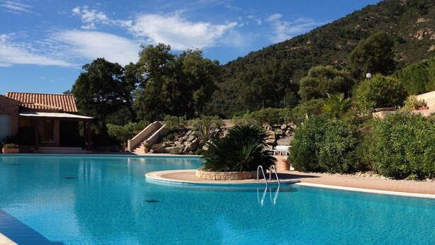 A clear blue swimming pool with a stone border, a metal ladder, and a view of a hillside with trees and a building in the background. - Well-kept apartment domaine with, pools, tennis. Pet friendly (Roquebrune-sur-Argens)