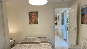 A bedroom with a bed, a chair, a door leading to a balcony, and a poster on the wall. - Well-kept apartment domaine with, pools, tennis. Pet friendly (Roquebrune-sur-Argens)