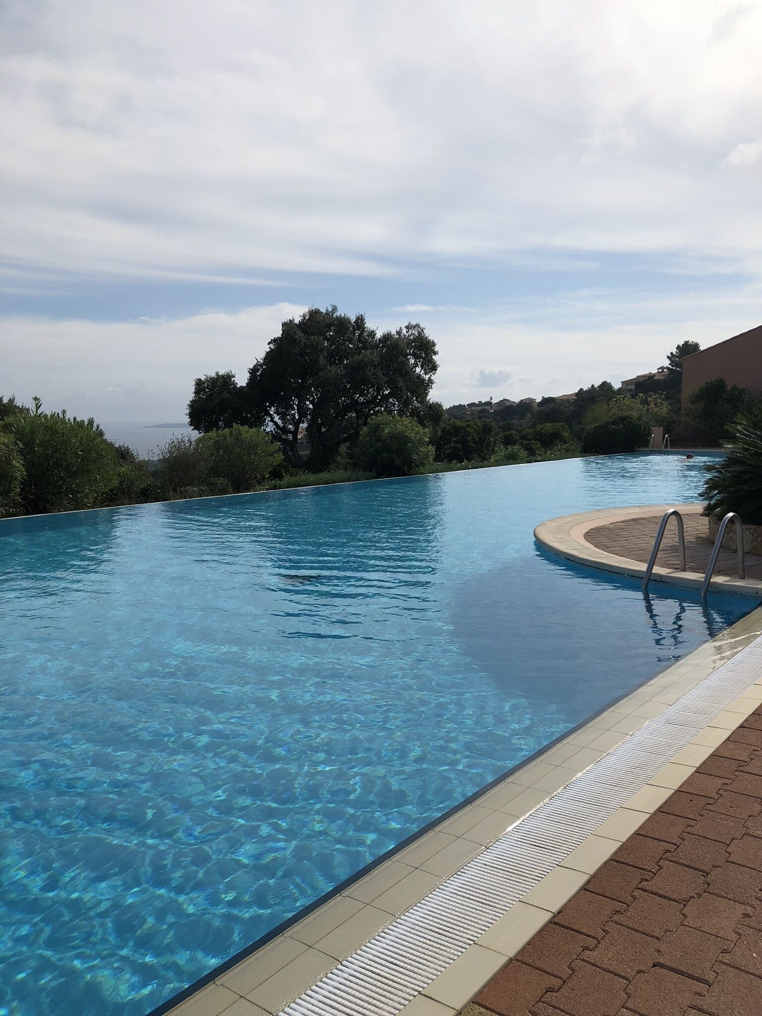 A clear swimming pool with a tiled edge, surrounded by greenery and a distant view of hills.