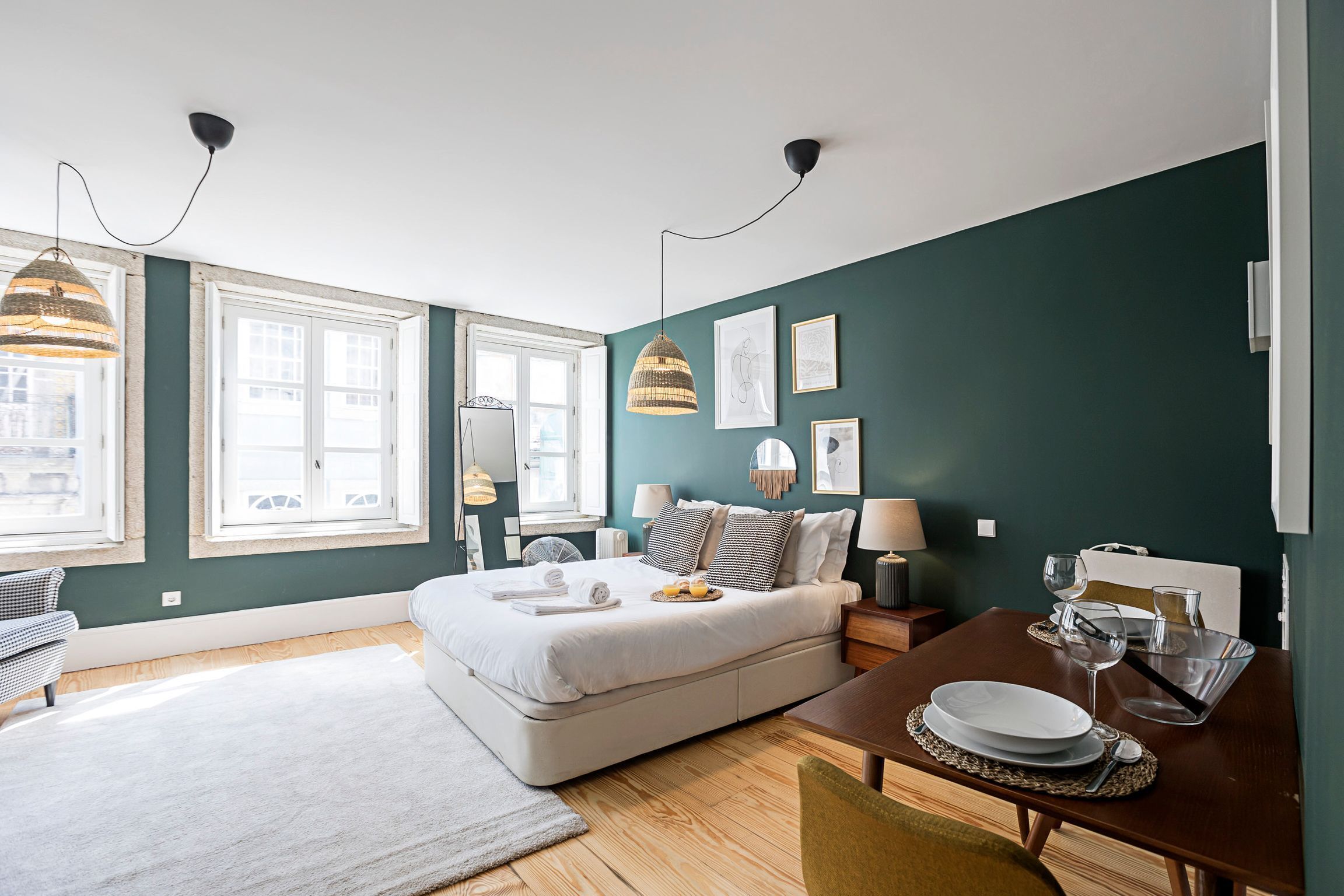 Un dormitorio moderno con cama, mesitas de noche, una mesa de comedor con sillas y ventanas amplias.