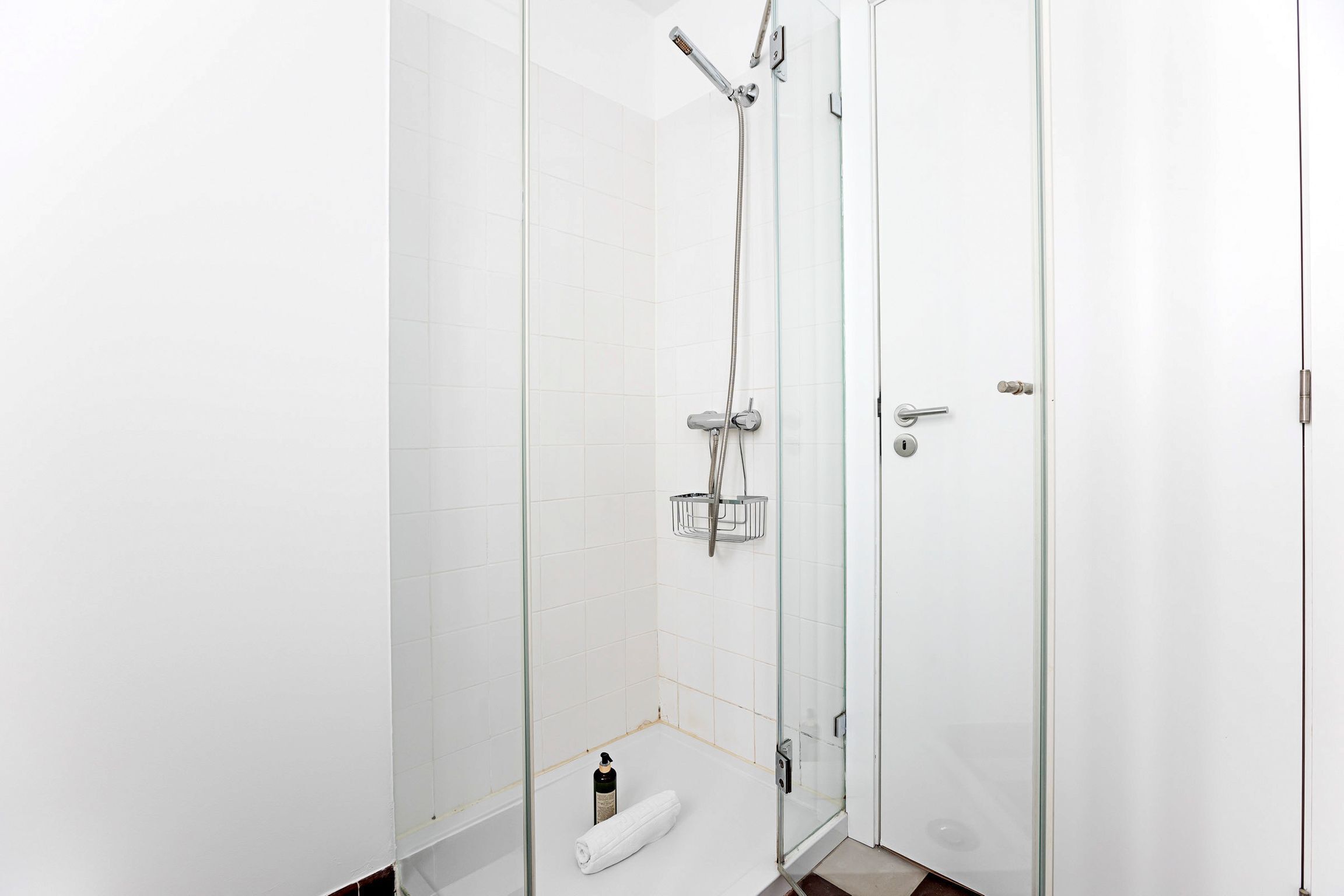 A modern bathroom with a glass-enclosed shower, white tiled walls, and a visible towel on the floor.