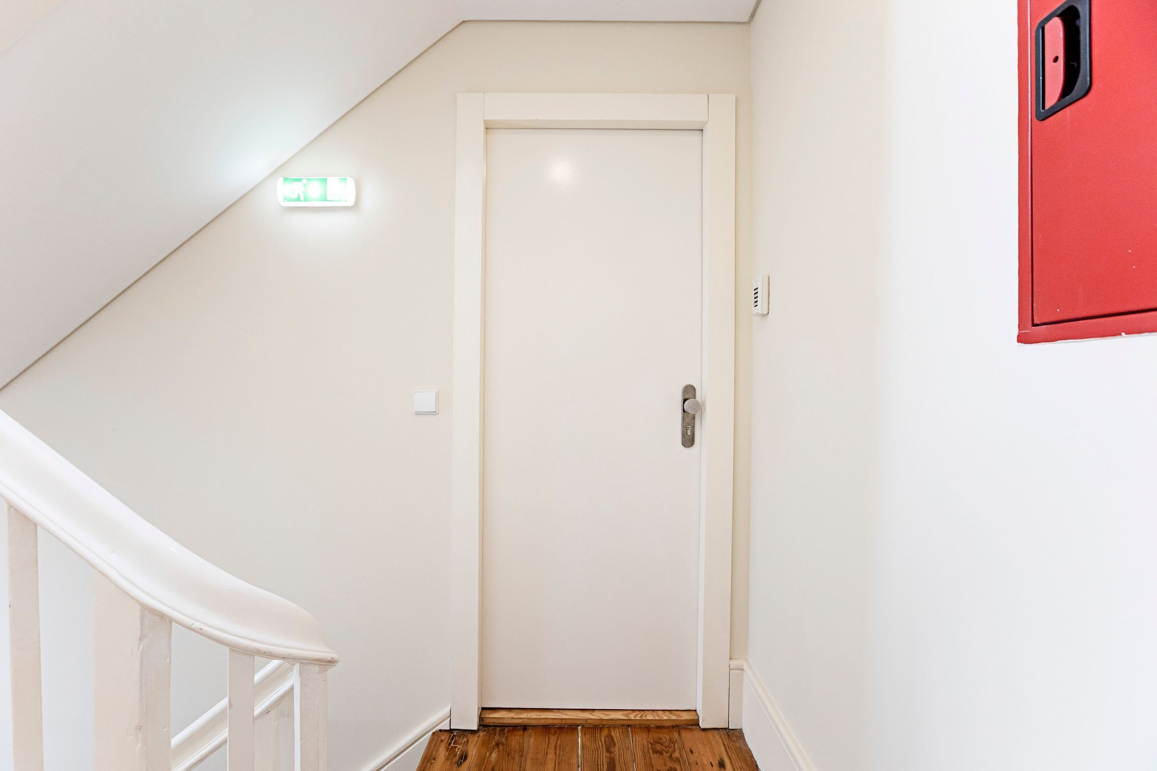 Una puerta blanca con manija, una pared blanca y un objeto rojo en la pared.