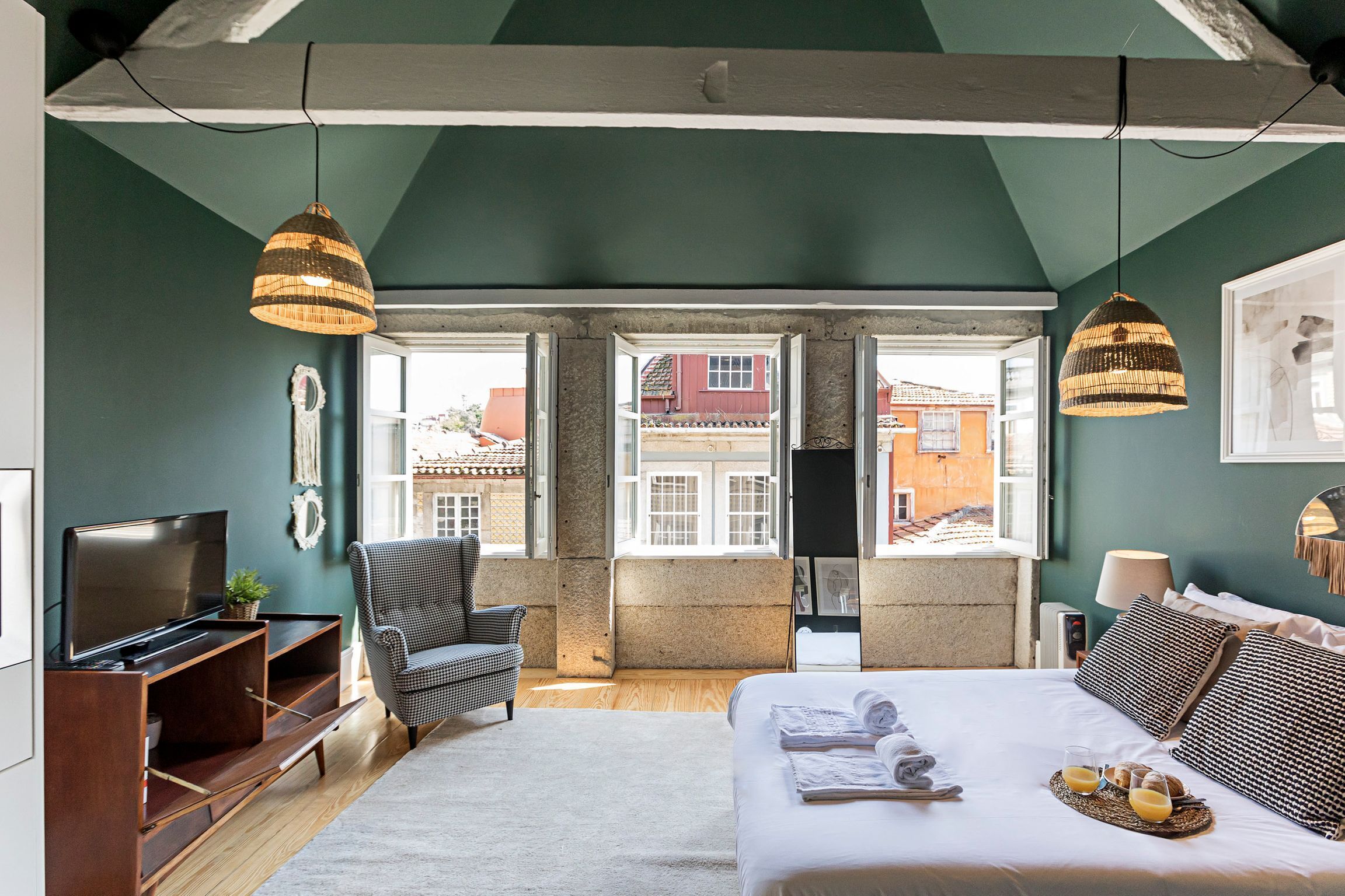 A bedroom with a bed, a TV, a chair, and a window with a view of buildings.