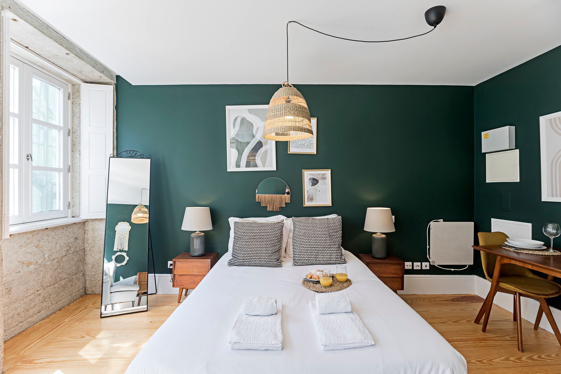 A neatly arranged bedroom with a large bed, bedside tables, a desk with a chair, and artwork on the walls.