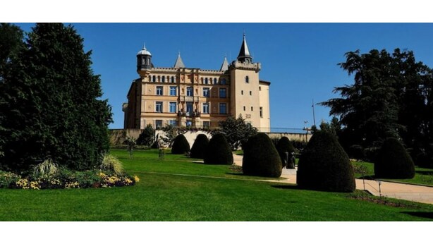 A large, historic building with multiple towers and a well-maintained garden with trimmed hedges and a pathway leading to the entrance. - Ideally located 70m2 T3 apartment with private balcony and secure parking (Saint-Priest)