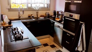 A modern kitchen with black cabinets, a gas stove, a dishwasher, and a window with curtains. - Ideally located 70m2 T3 apartment with private balcony and secure parking (Saint-Priest)