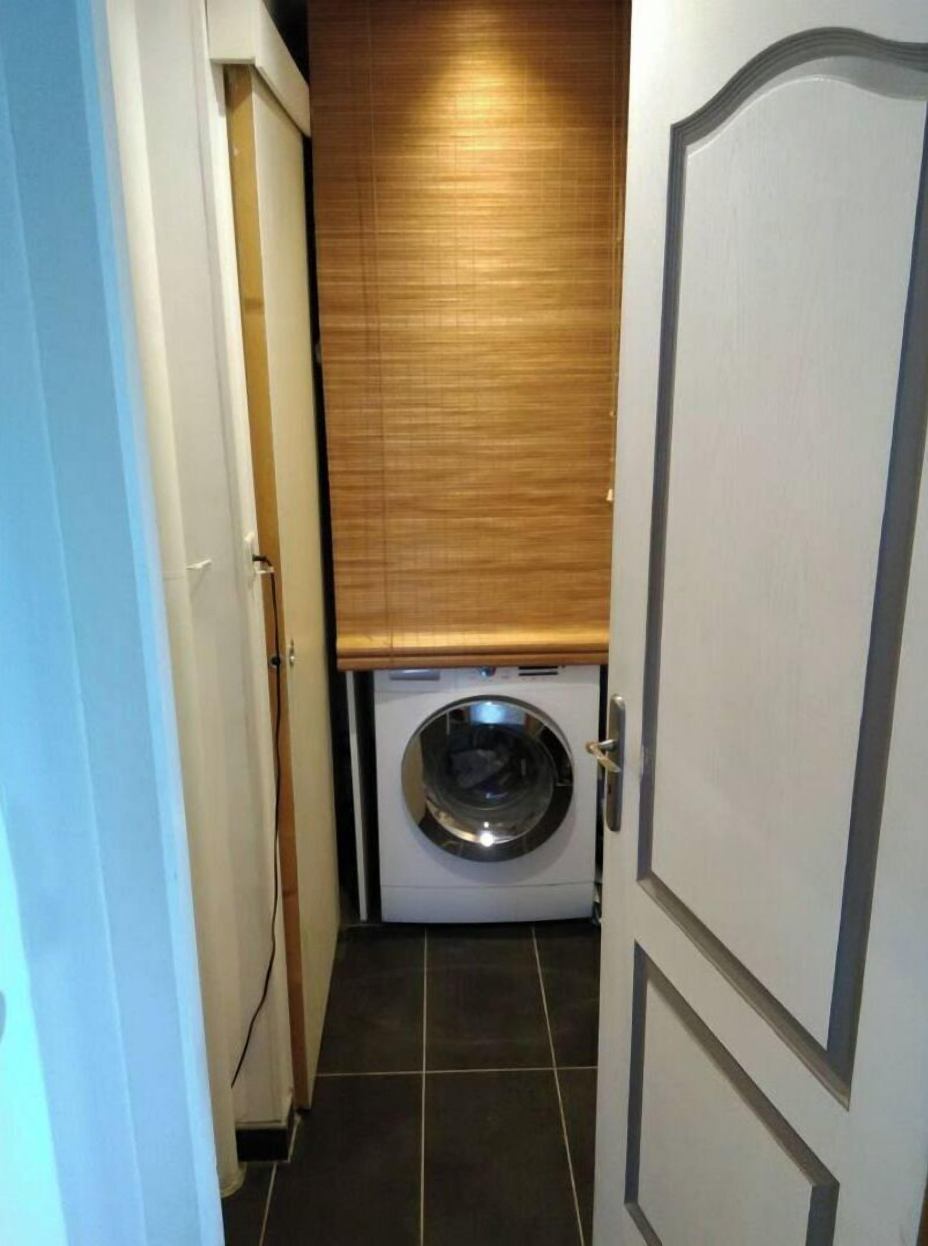Une buanderie équipée d’un lave-linge, dotée d’une porte en bois et d’un sol carrelé.