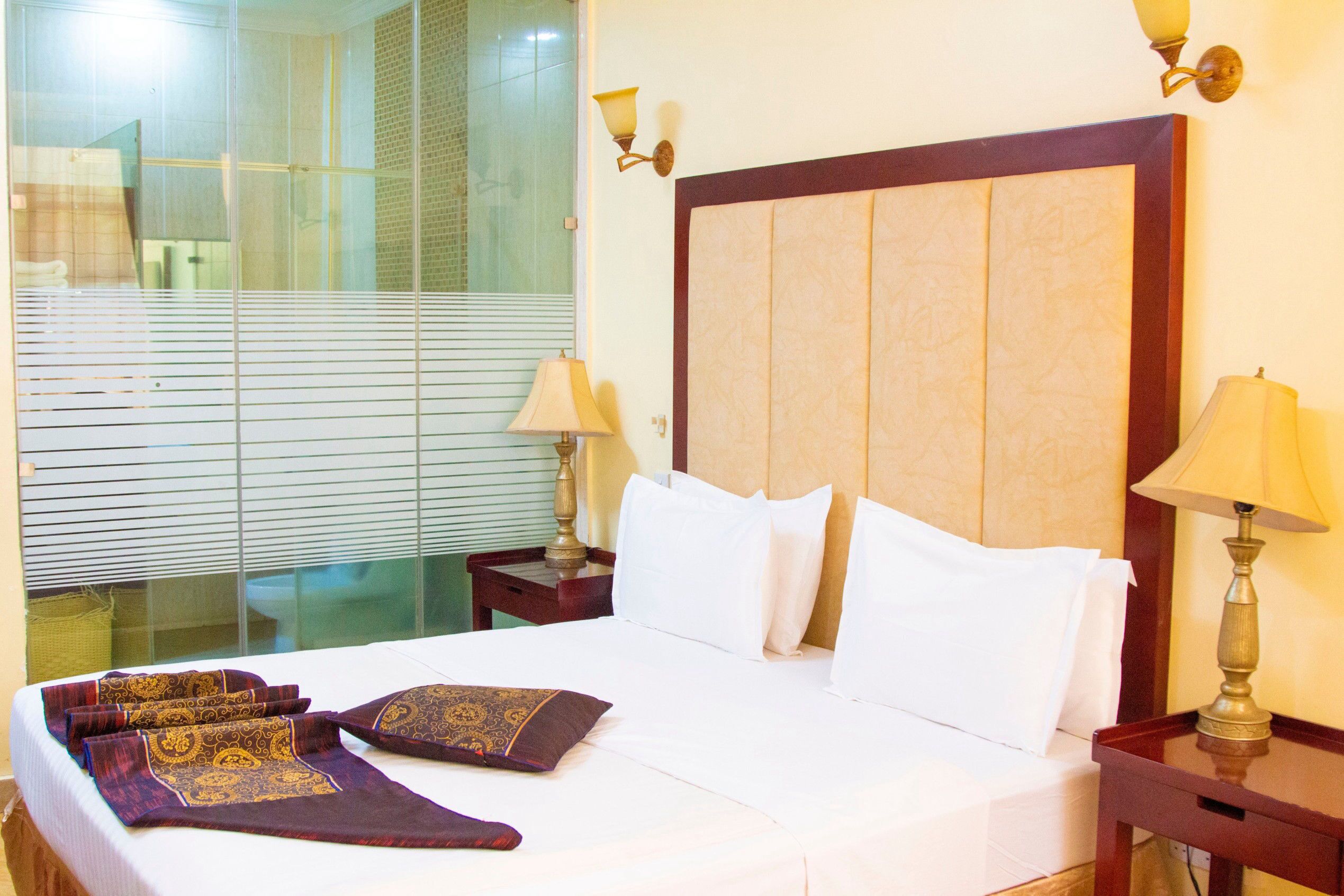 A hotel room with a large bed, two bedside tables, and a window with blinds.