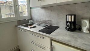 Una cocina con un lavamanos, un escurreplatos, una cafetera y armarios.