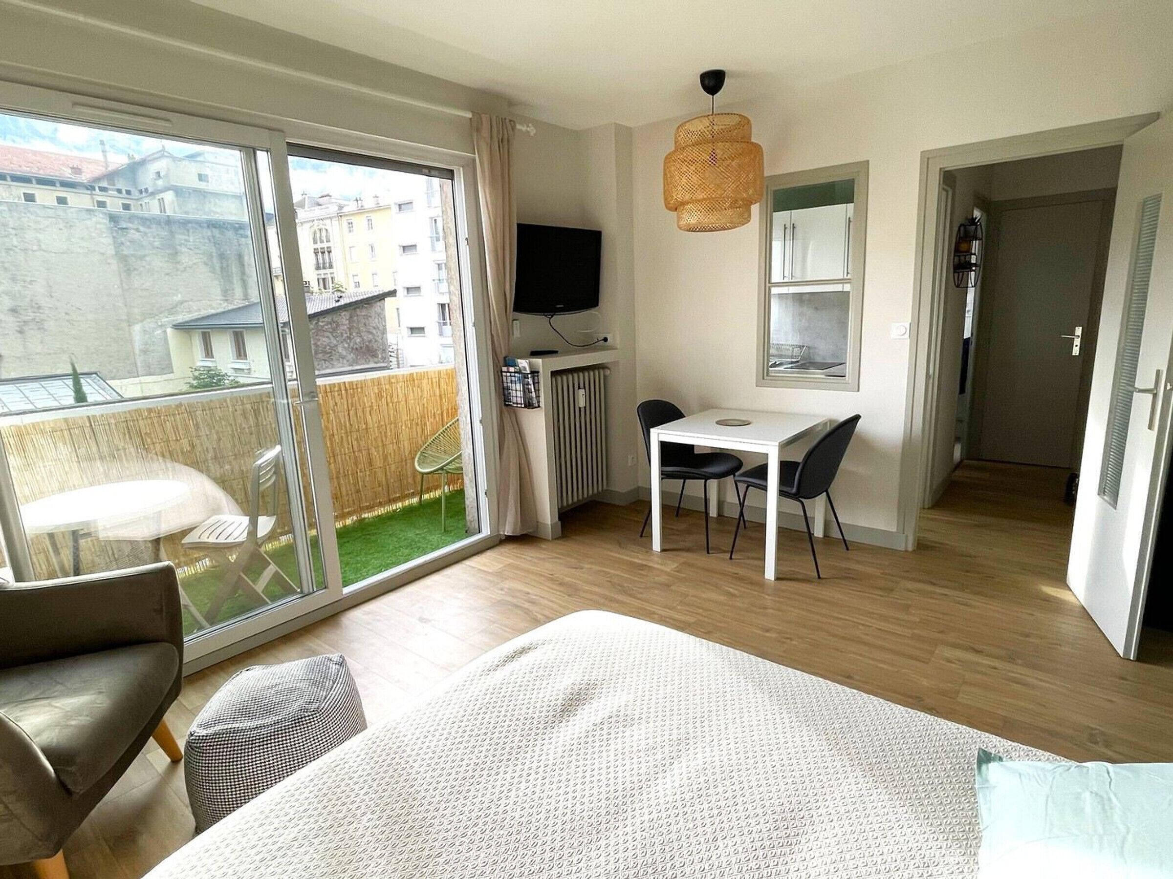 A bedroom with a bed, a desk, and a chair, a balcony with a table and chairs, and a TV.