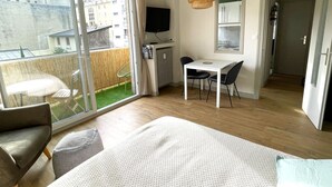 Un dormitorio con cama, escritorio, silla, un balcón con mesa y sillas, y una televisión.