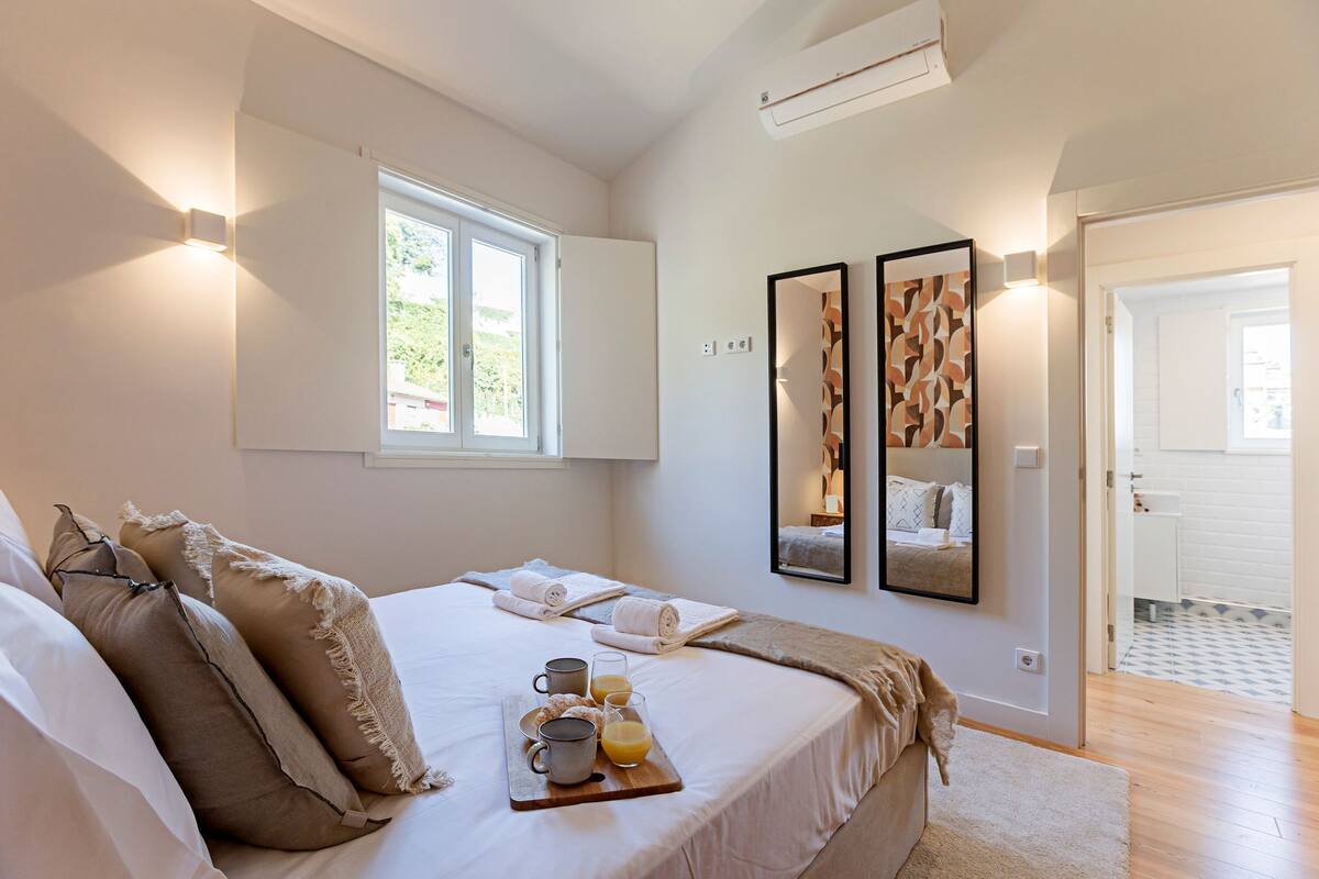 A bedroom with a bed, towels, a tray with mugs and juice, and two framed pictures on the wall.