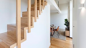 Uma escada de madeira com design moderno, dando acesso a uma sala de jantar com mesa e cadeiras.