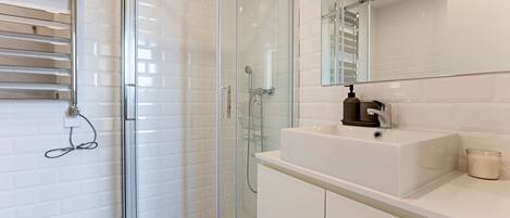 A modern bathroom with a glass-enclosed shower, white tiled walls, a white sink with a mirror above, and a small towel rack.