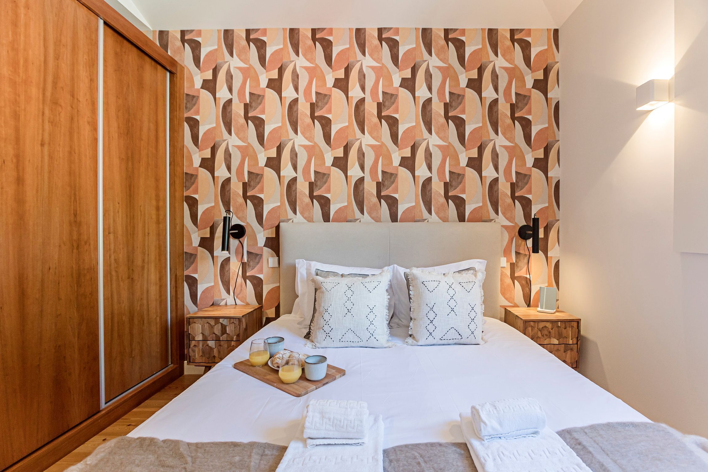 Una cama bien hecha con almohadas, una mesita de noche con lámpara y un armario de madera.