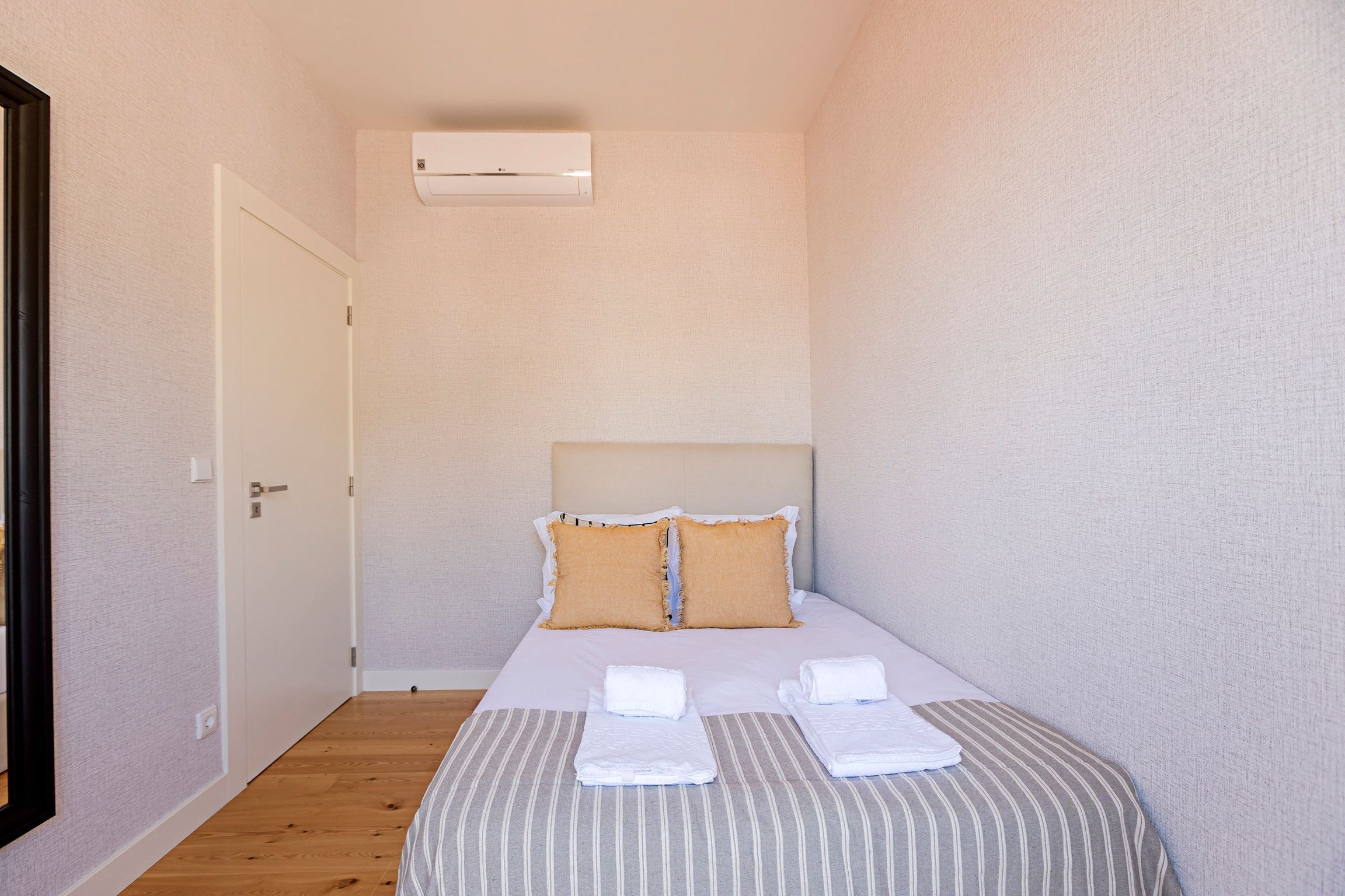 Ein kleines, ordentlich eingerichtetes Hotelzimmer mit einem Einzelbett, einem Kopfteil und einem Fenster.