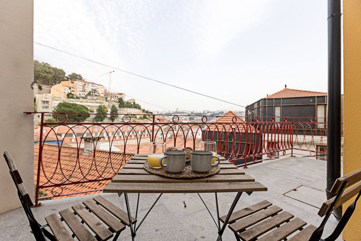 A balcony with a table set for two, a metal railing, and a view of buildings in the background.