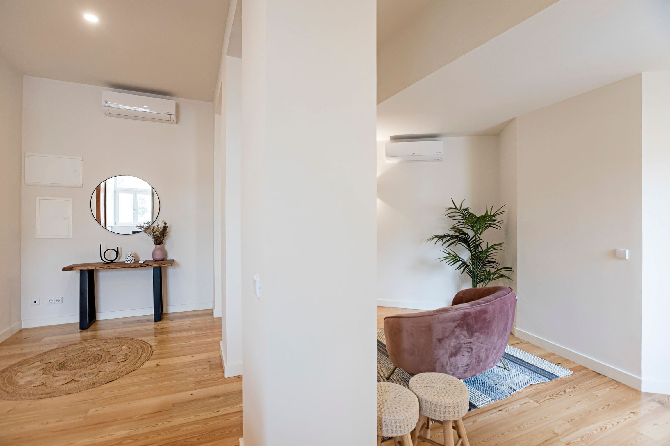 Ein modernes Interieur mit Holzboden, einem runden Spiegel, einer Bank und einem Blumentopf.