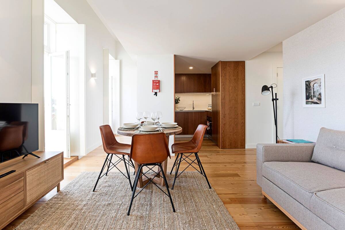 A modern living room with a dining area, wooden flooring, and a grey sofa.