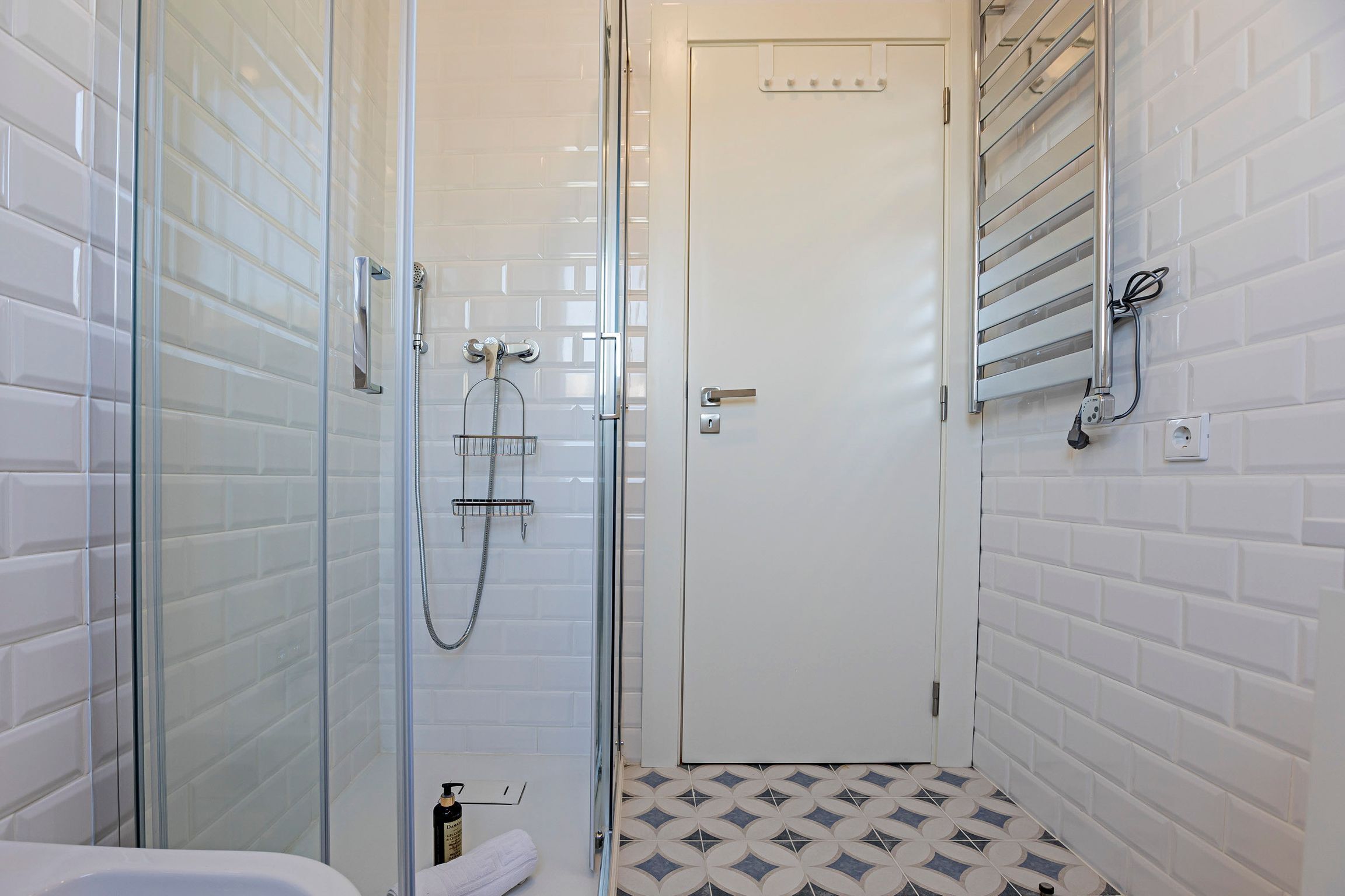 A modern bathroom with a glass-enclosed shower, a white door, and a patterned floor.