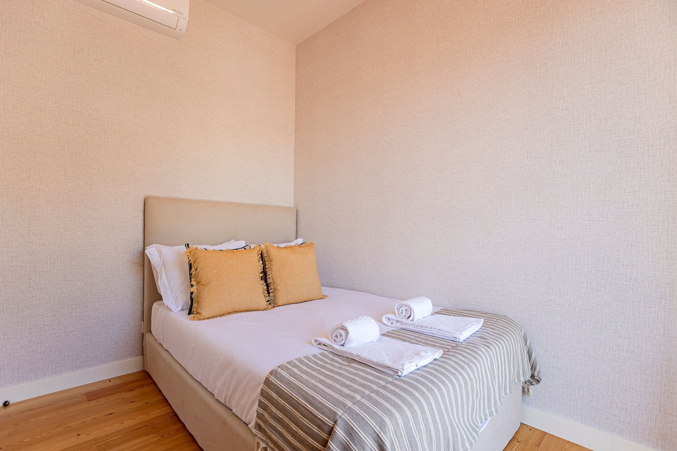 A neatly made bed with striped bedding, two pillows, and two rolled towels.