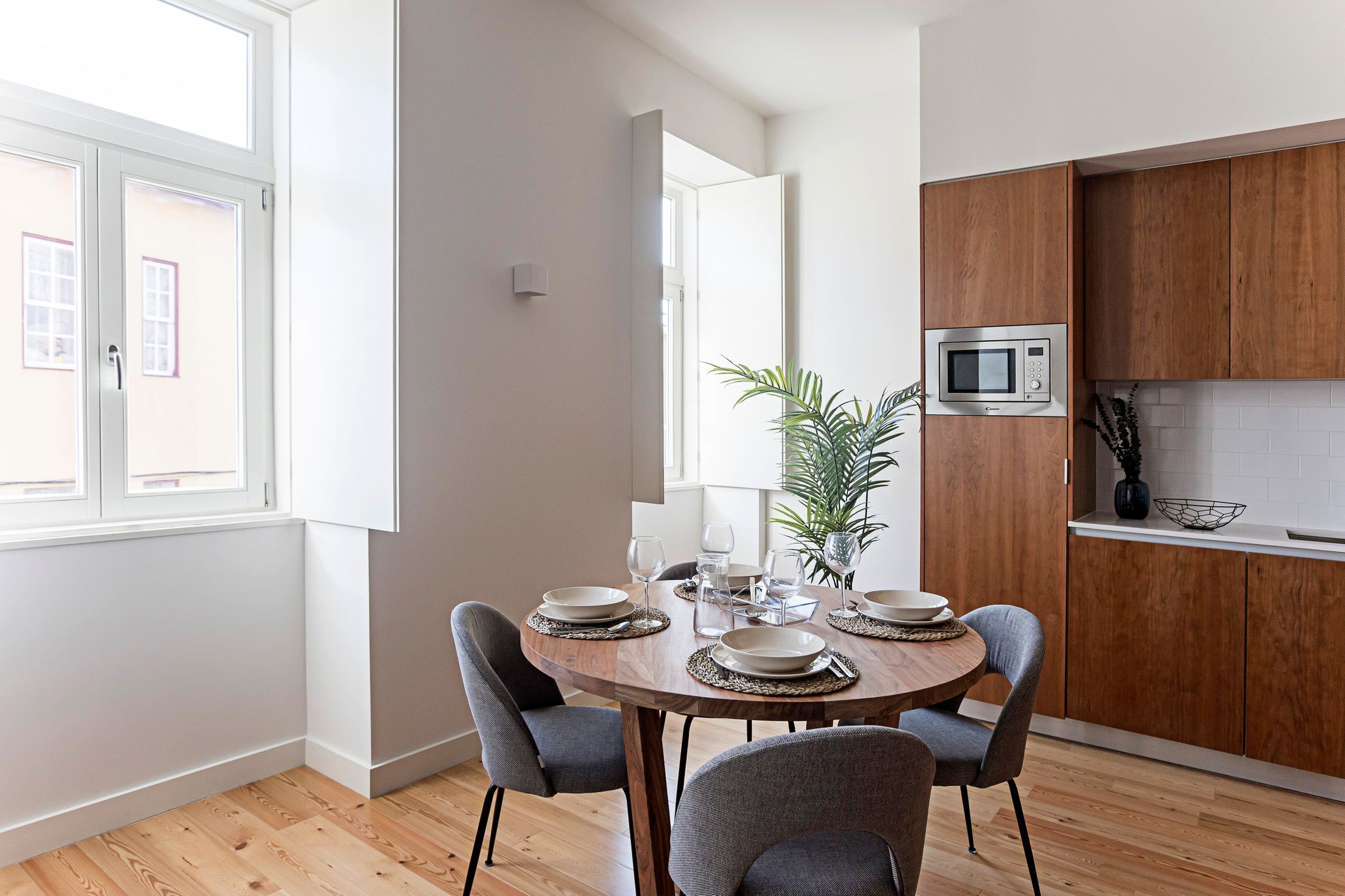 Una cocina moderna con armarios de madera, un microondas y un comedor con una mesa redonda y cuatro sillas.