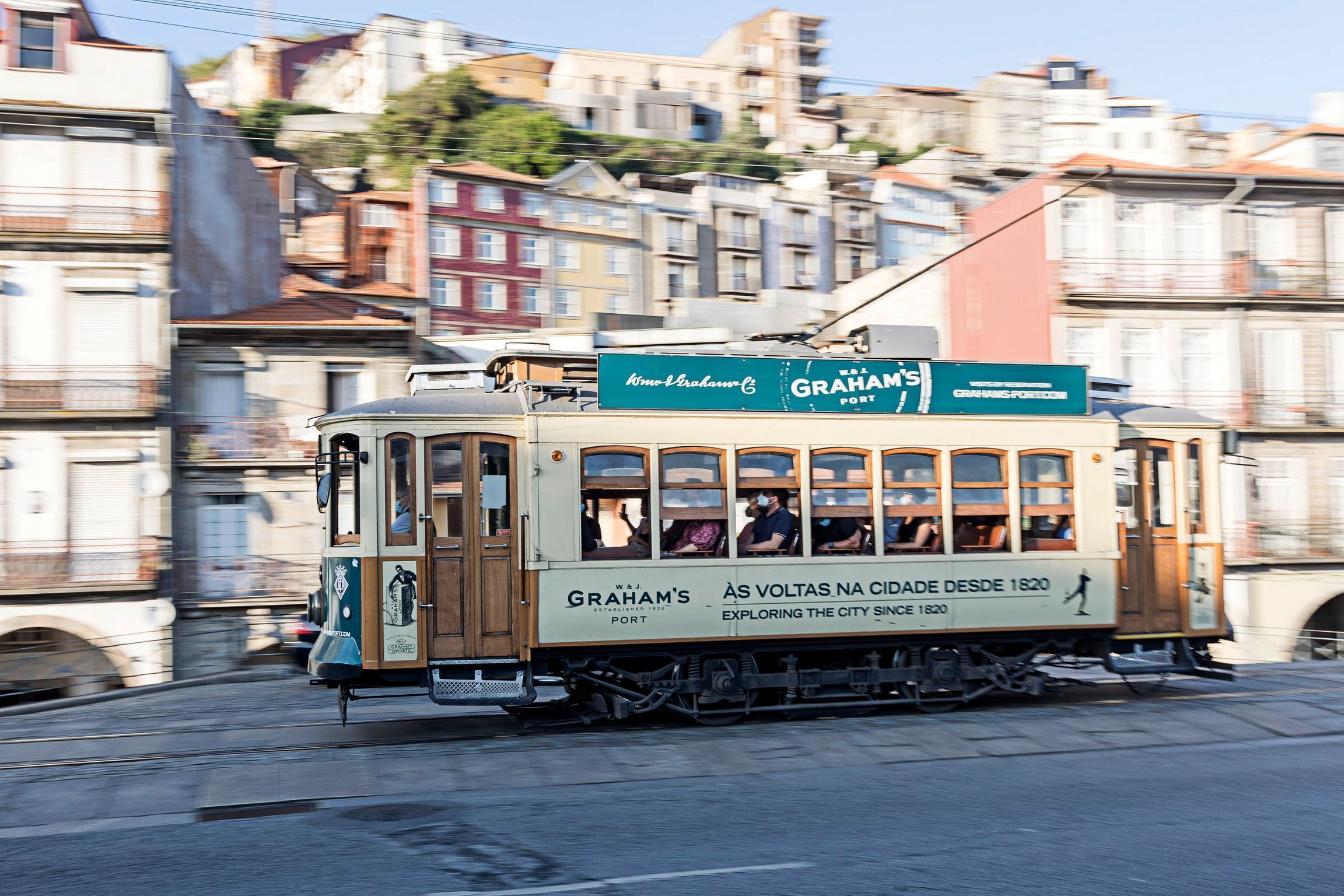 A vintage tram with "Graham's" branding, traveling through a city with historic buildings in the background.