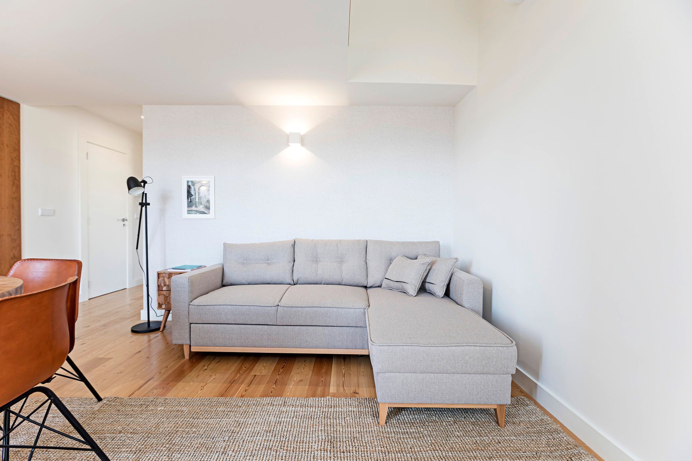 A modern living room with a grey sectional sofa, a wooden floor, and a floor lamp.