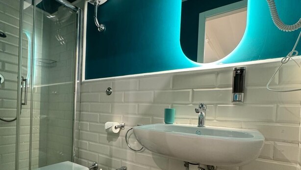 A modern bathroom with a glass shower enclosure, a white toilet, a bidet, and a white sink with a mirror above it. - Le Petit Bijou (Rome)