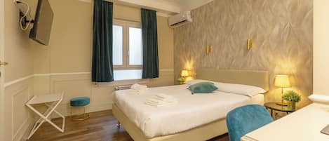 Habitación de hotel con cama, una mesita, una silla, ventana con cortinas, unidad de aire acondicionado y lámpara de pared.