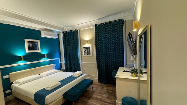 A modern hotel room with a large bed, a desk with a mirror, and a small seating area. - Le Petit Bijou (Rome)