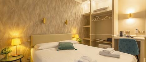 A hotel room with a bed, bedside lamps, a desk with a chair, a wardrobe, and a small table with a plant.