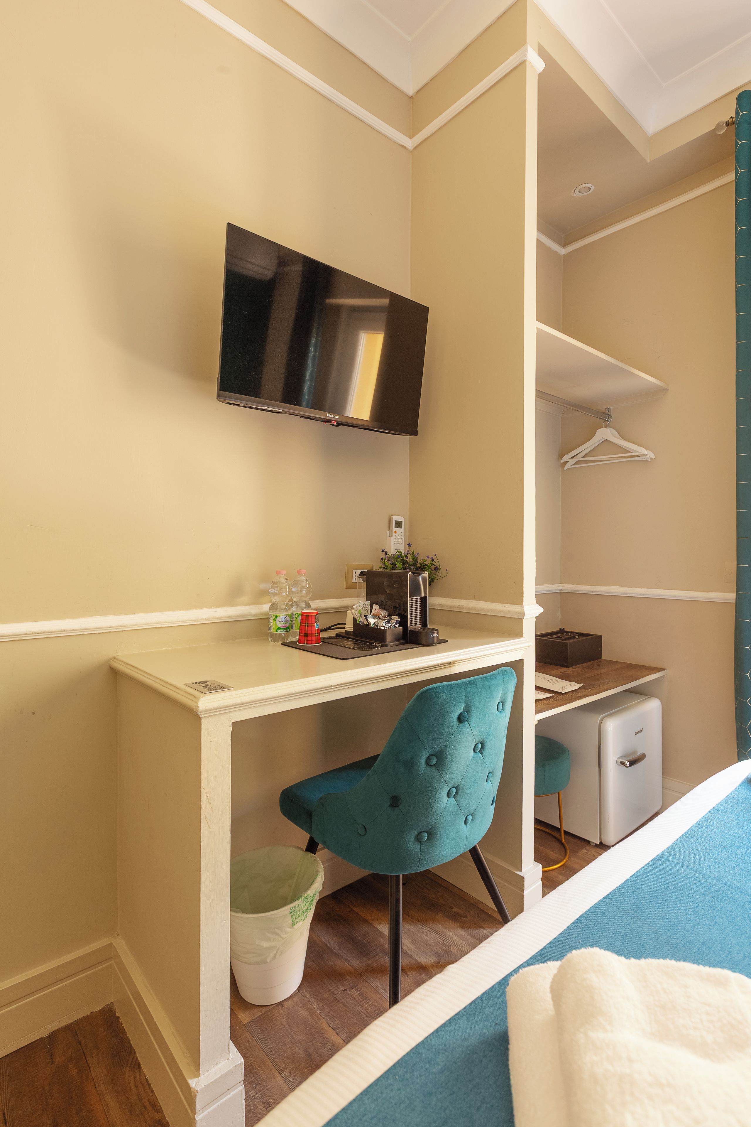 A bedroom with a bed, a desk with a chair, a TV, and a small kitchenette.