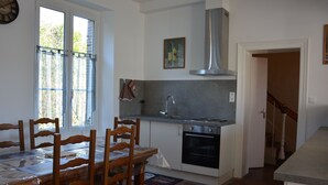 A kitchen with a dining table, chairs, a stove, oven, and a window with curtains.