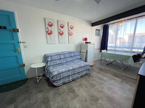 A room with a blue door, a sofa, a small table, a cabinet, and a window with a view.