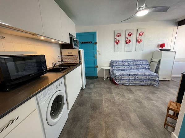 A compact kitchen with a microwave, washing machine, and a small table.