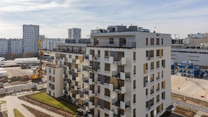 A multi-story residential building with balconies, a construction crane in the background, and a clear sky.