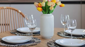 A dining table set with white plates, clear wine glasses, and a white vase with yellow and orange tulips.