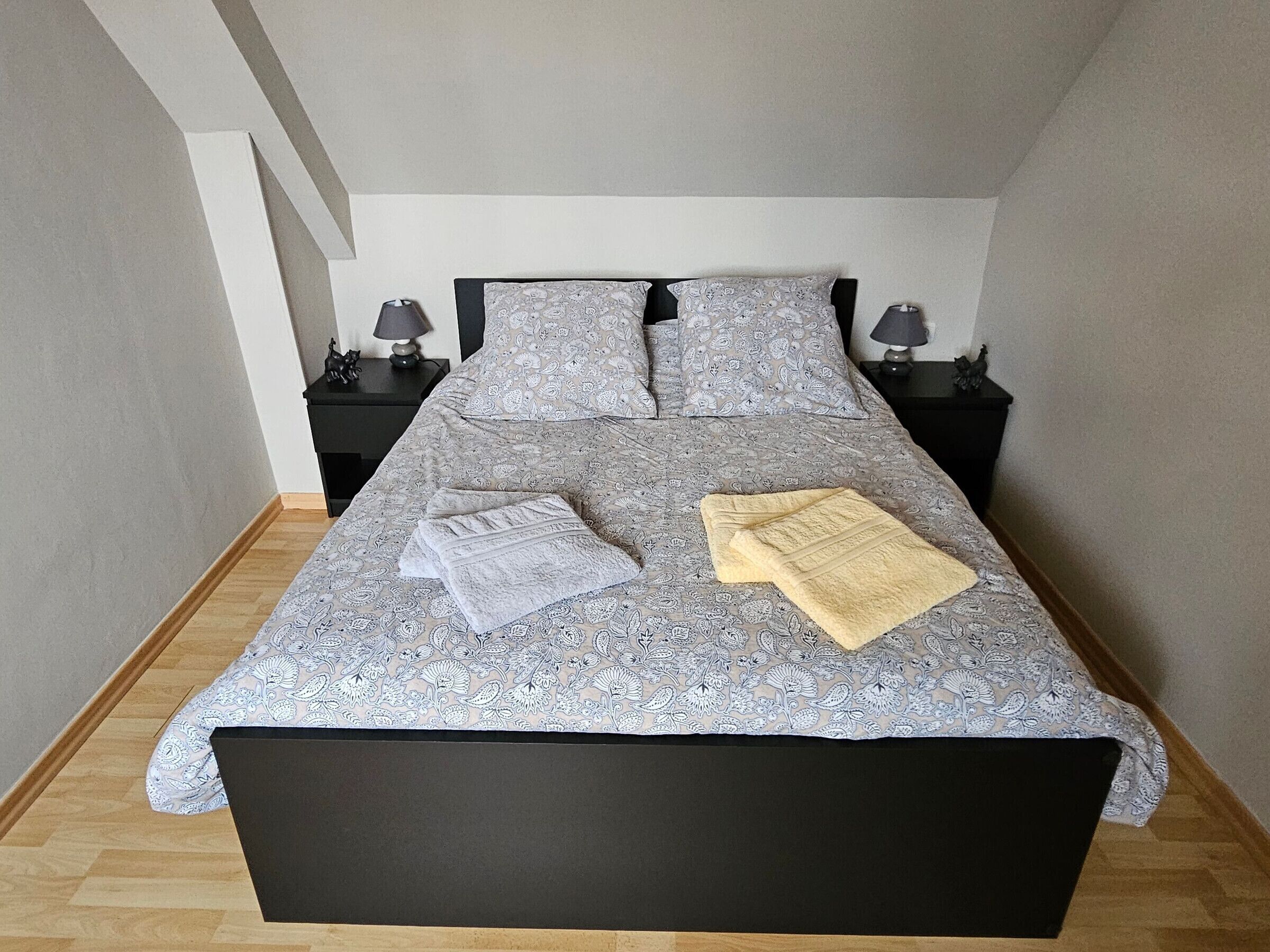 A neatly made bed with patterned bedding, two bedside tables with lamps, and a wooden floor.
