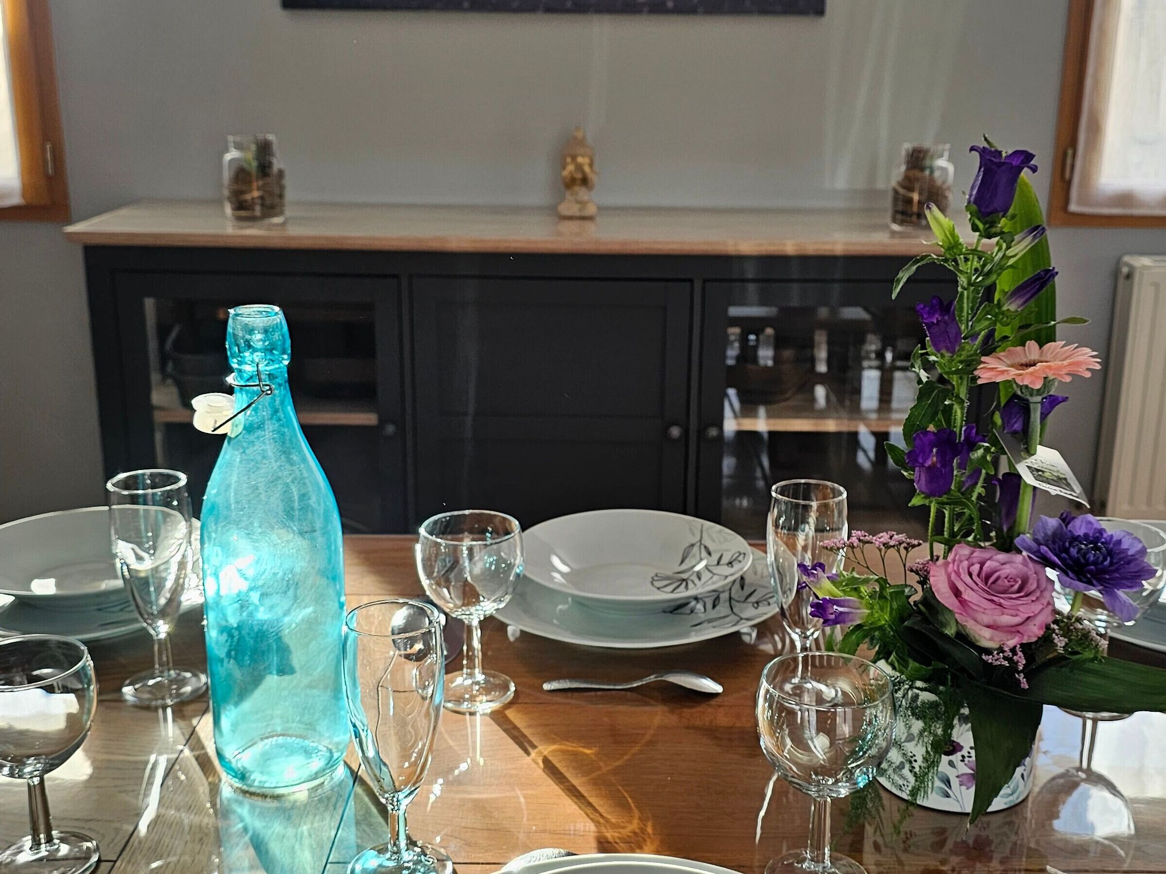 A dining table set with plates, glasses, a bottle, and a floral centerpiece.