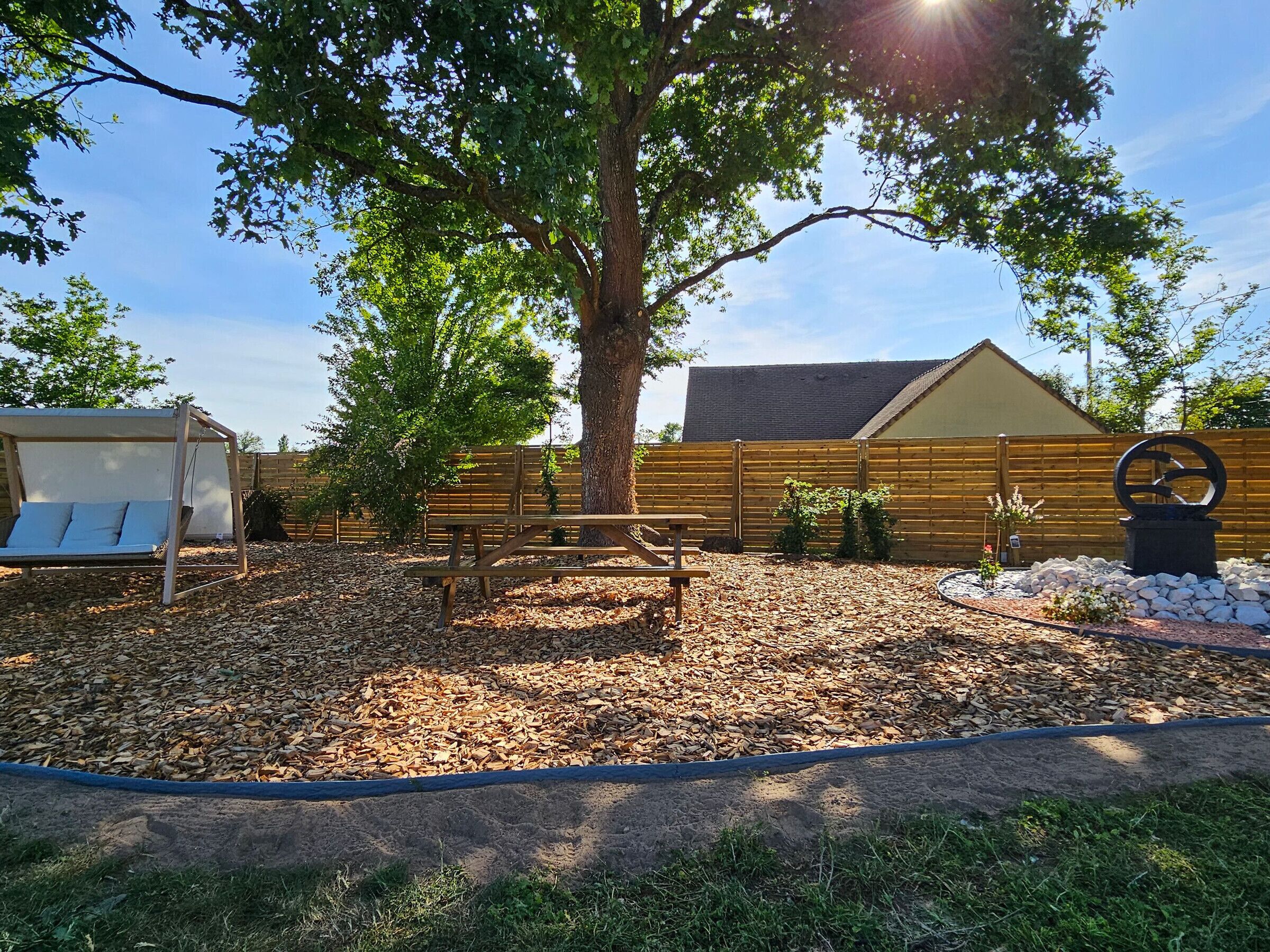 A patio area with a swing, a picnic table, and a large tree.